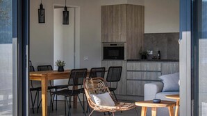Una cocina moderna con horno empotrado y microondas, un comedor con mesa de madera y sillas de mimbre, y un sofá gris en la sala.