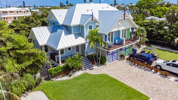 A large, multi-story house with a distinctive roof design, surrounded by lush greenery and a well-maintained lawn.