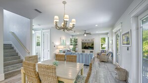 A spacious living area with a dining table, wicker chairs, a chandelier, and a television.