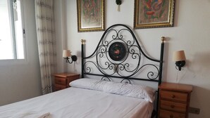 Una cama bien hecha con ropa de cama blanca y una toalla doblada, dos mesitas de noche con lámparas, y dos obras de arte enmarcadas en la pared.