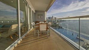 Un balcón con una mesa y sillas para comer, con vistas a una piscina y al horizonte de la ciudad.