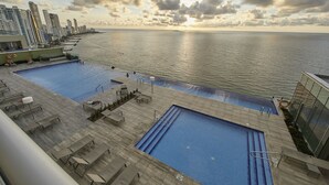 Piscina en la azotea con vistas a la ciudad, sillas de descanso y cielo despejado.