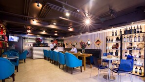 Een restaurant met blauwe stoelen, een bar en wijnflessen op rekken.