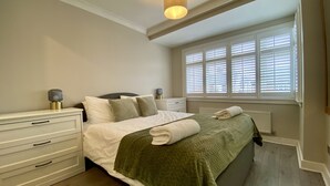A bedroom with a bed, bedside tables, a window with blinds, and a ceiling light fixture.