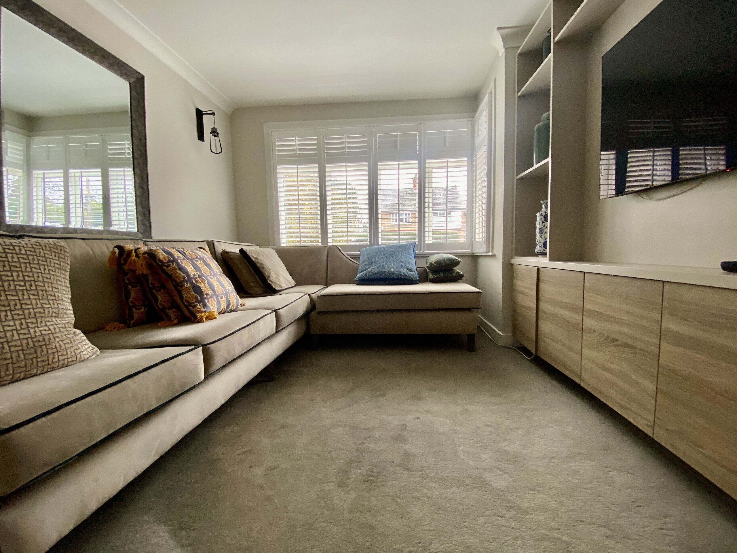 A living room with a beige sofa, a blue pillow, and a large mirror on the wall.