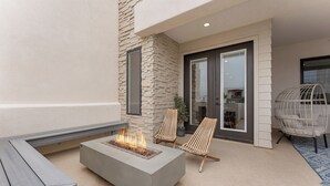 A modern outdoor seating area with a fire feature, two wicker chairs, and a unique hanging chair. - Sandstone Shores: Desert Color Lagoon + Beaches (St. George)