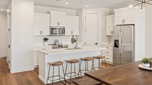 A modern kitchen with white cabinetry, a central island with stools, stainless steel appliances, and a wooden dining table. - Sandstone Shores: Desert Color Lagoon + Beaches (St. George)
