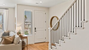 A well-lit entryway with a wooden floor, a white door, a staircase with black railings, and a window with blinds. - Sandstone Shores: Desert Color Lagoon + Beaches (St. George)