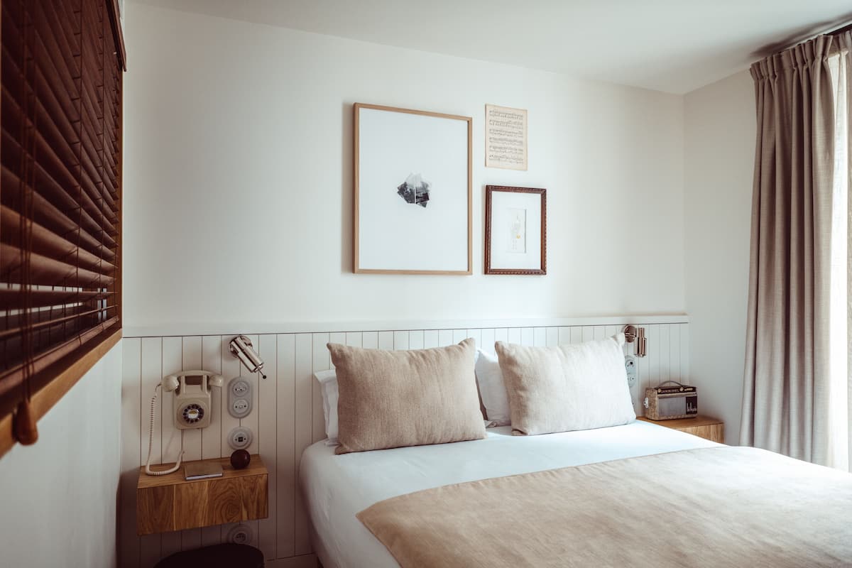 Una habitació d'hotel amb un llit, una taula de nit amb un telèfon, una ràdio i un quadre al mur.
