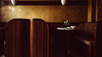 Un restaurante tenuemente iluminado con cabinas de madera, una pequeña mesa con una vela y un aplique de pared.
