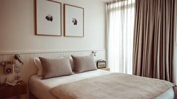 Ein ordentlich eingerichtetes Schlafzimmer mit einem Bett, zwei Kissen, einem Nachttisch mit Lampe, einem Radio und gerahmten Bildern an der Wand.