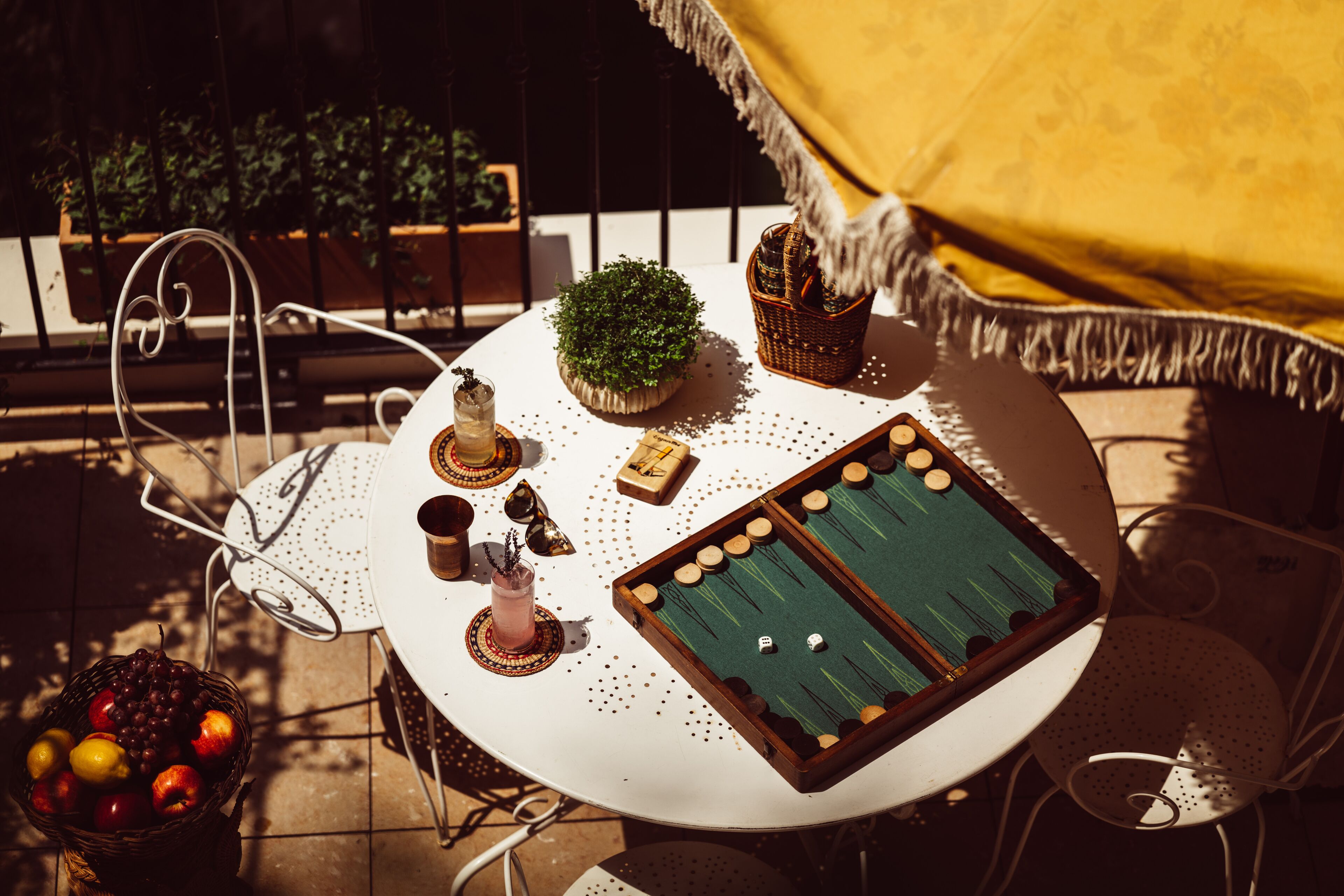 Ein runder Tisch mit einem grünen Spieltischfilz, einem kleinen Topf mit Pflanze, einem Korb und einem Glas mit Getränk.