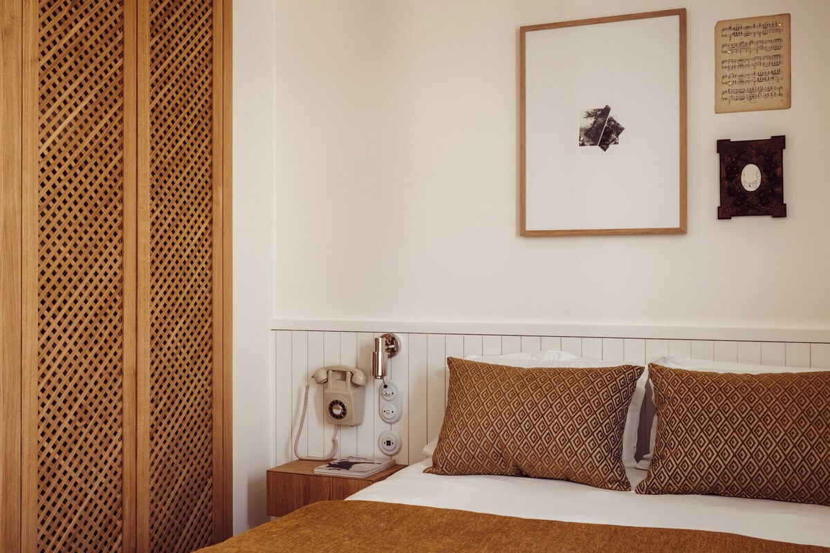 A bedroom with a bed, wooden wardrobe, bedside table, and a wall-mounted telephone.