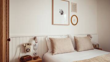 Een netjes ingerichte slaapkamer met een bed, nachtkastjes, een telefoon en ingekaderde foto's aan de muur.