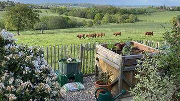 Un paysage rural avec un pré délimité par une clôture, une terrasse en bois et un jardin agrémenté de fleurs et de plantes.