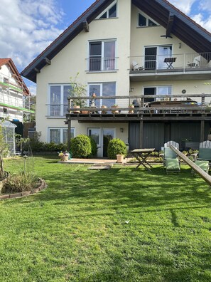 A two-story residential building with a balcony, a garden, and outdoor furniture.
