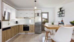 A modern kitchen with white cabinets, a stainless steel refrigerator, and a wooden dining table with white chairs.