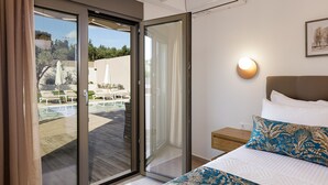 A bedroom with a bed, a nightstand, a wall-mounted lamp, and a sliding glass door leading to an outdoor area with a pool and lounge chairs.