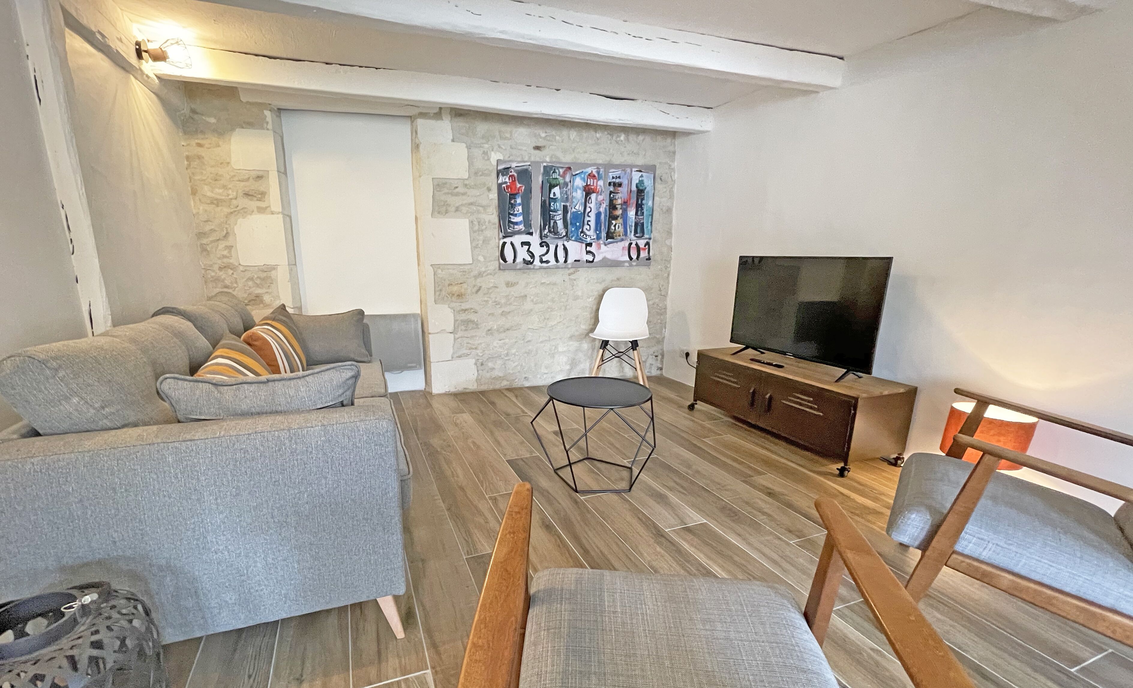Un salon avec un canapé gris, une table basse en bois, un téléviseur posé sur un meuble en bois et un mur orné d’un tableau.
