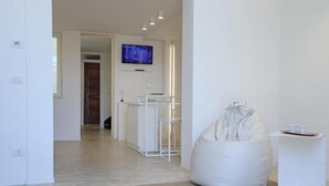 Una habitación moderna y minimalista con un sillón tipo bean bag blanco, una mesita con tazas y un televisor de pantalla plana montado en la pared.