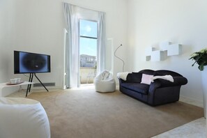 A modern living room with a flat-screen TV on a stand, a dark blue sofa, a white bean bag chair, and a white coffee table.