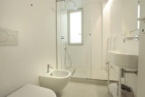 A modern bathroom with a bidet, a glass-enclosed shower, and a large mirror.