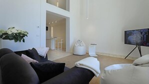 Una sala de estar moderna con un sofá negro, un sillón de peluche blanco y un televisor de pantalla plana sobre un mueble.
