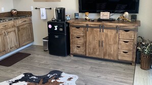 Une cuisine moderne avec des meubles en bois, un réfrigérateur noir, une machine à café et un téléviseur à écran plat fixé au mur.