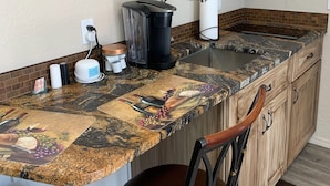 Une cuisine avec des meubles de rangement en bois, un plan de travail en granit, une machine à café, un grille-pain et une chaise.