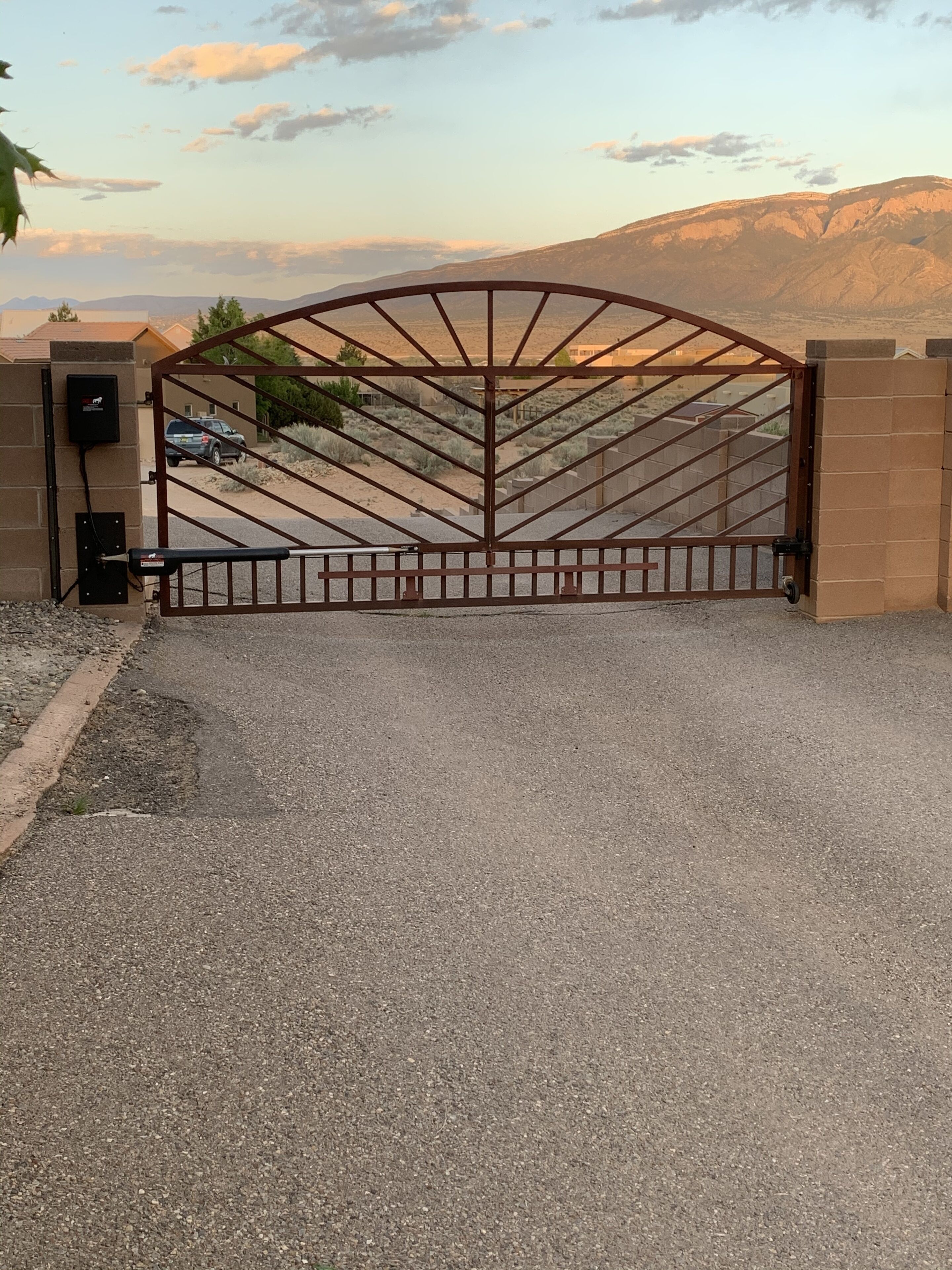 A gated entrance with a metal gate and a control box on the wall.