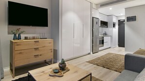 Uma sala de estar moderna com televisão de tela plana, móveis de madeira e uma área de cozinha ao fundo.