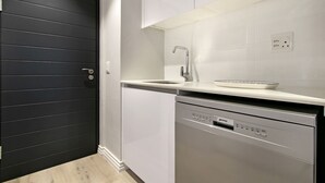 Cozinha moderna com porta preta, armários brancos, lava-louças de aço inoxidável e bancada branca com pia.