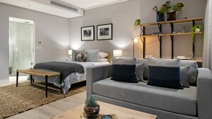 Uma sala de estar moderna com um sofá cinza, um banco de madeira, uma mesa de centro e uma estante com plantas.