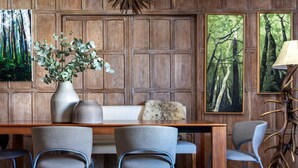 A dining area with a wooden table, four chairs, a vase with greenery, and two framed paintings of forests. - Cockspur Street by onefinestay (London)