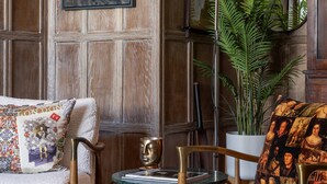 A room with a wooden paneled wall, a framed cityscape painting, a floor lamp, a potted plant, and a patterned rug. - Cockspur Street by onefinestay (London)