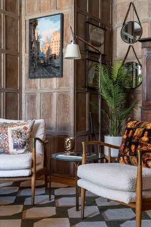 A room with a wooden paneled wall, a framed cityscape painting, a floor lamp, a potted plant, and a patterned rug. - Cockspur Street by onefinestay (London)
