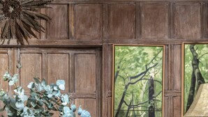 A wooden dining area with a table, chairs, a vase with foliage, a painting of a forest, and a decorative lamp. - Cockspur Street by onefinestay (London)