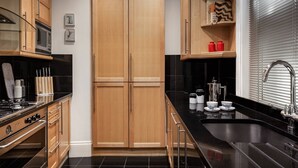 A modern kitchen with black countertops, wooden cabinets, a built-in oven, and a stainless steel sink. - Cockspur Street by onefinestay (London)