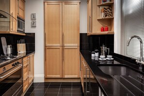 A modern kitchen with black countertops, wooden cabinets, a built-in oven, and a stainless steel sink. - Cockspur Street by onefinestay (London)