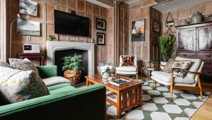 A living room with a fireplace, green sofa, armchairs, and a television mounted on the wall. - Cockspur Street by onefinestay (London)