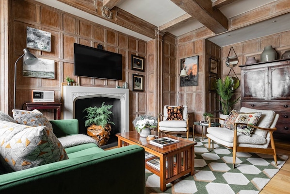A living room with a fireplace, green sofa, armchairs, and a television mounted on the wall.