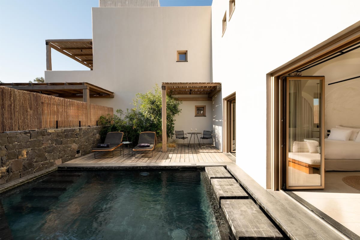 A modern outdoor pool area with lounge chairs, a wooden deck, and a stone wall.