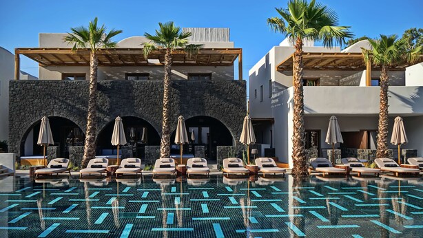 A pool area with lounge chairs and umbrellas, surrounded by palm trees and modern architecture.