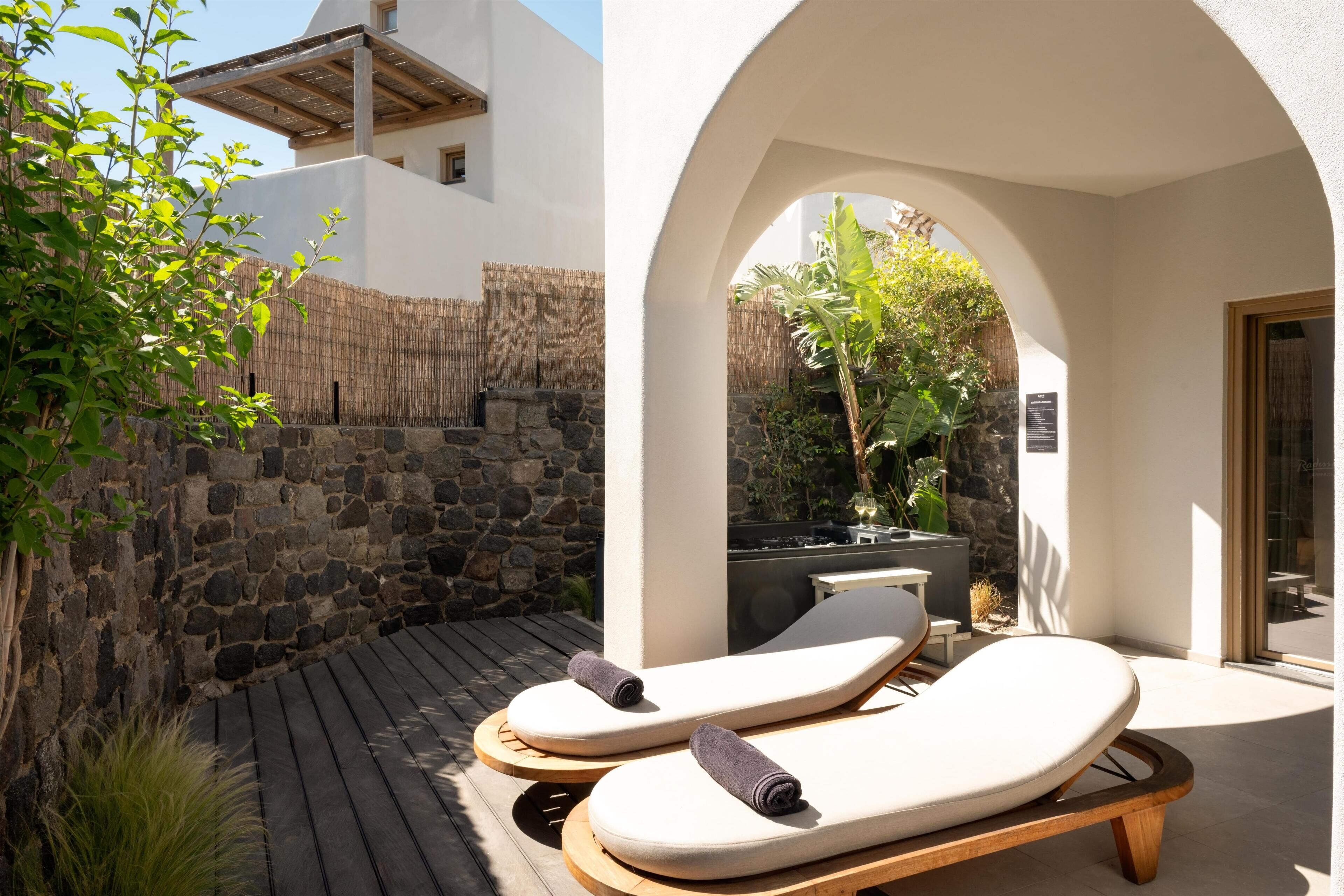 A sunlit outdoor seating area with lounge chairs and a stone wall.