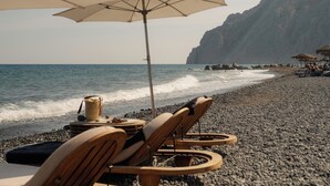 A beach with wooden lounge chairs and umbrellas, a rocky shoreline, and a cliff in the background.
