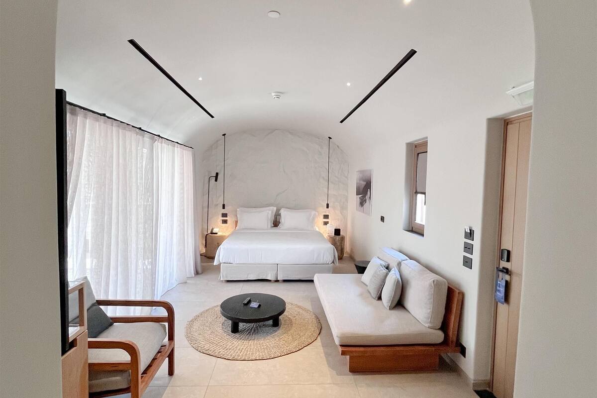 A modern hotel room with a large bed, a sofa, a coffee table, and a TV.
