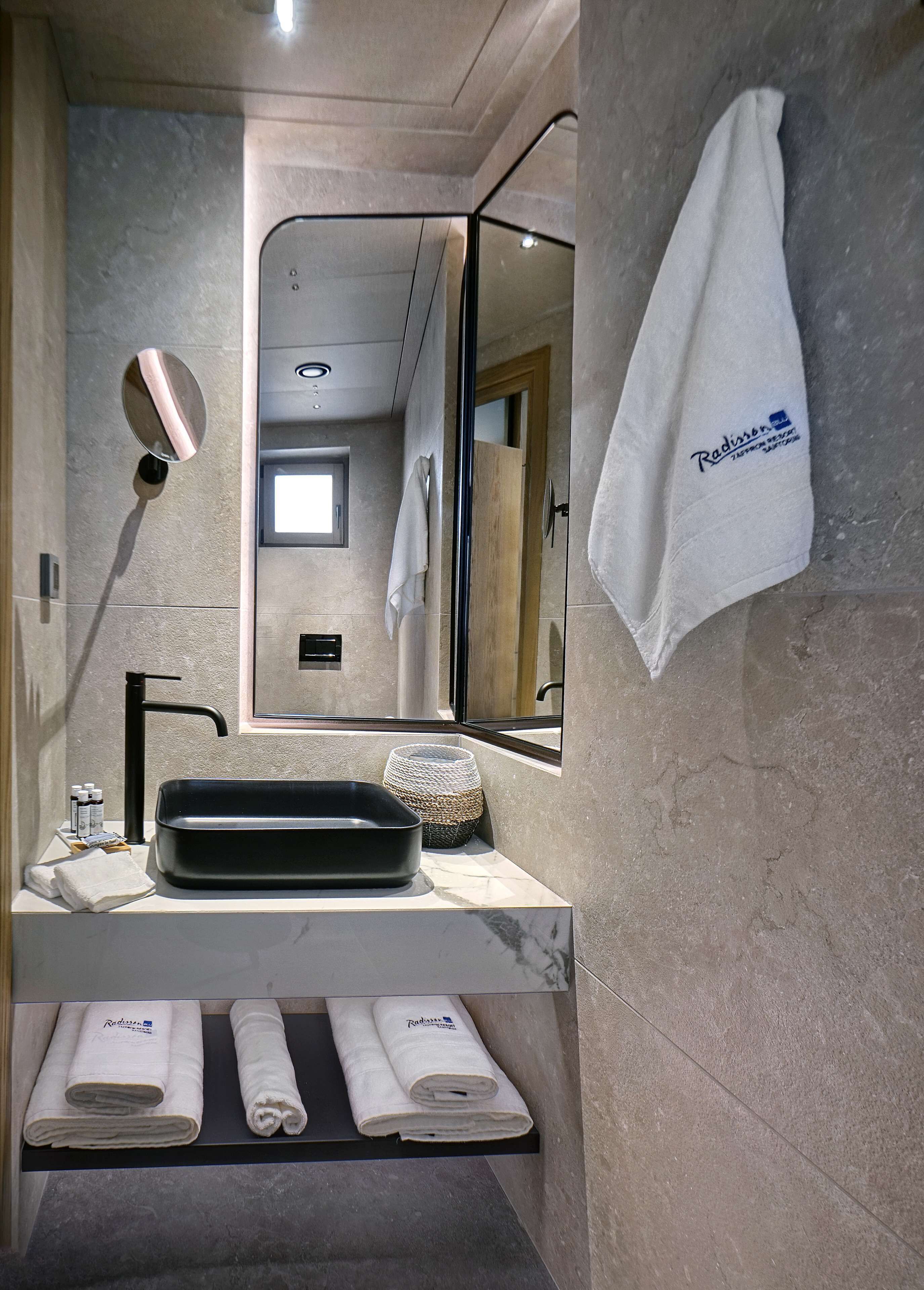 Une salle de bain moderne avec un grand miroir, un lavabo noir et un porte-serviettes avec des serviettes blanches.