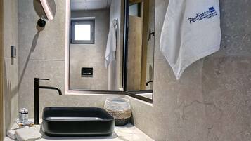 Une salle de bain moderne avec un grand miroir, un lavabo noir et un porte-serviettes avec des serviettes blanches.