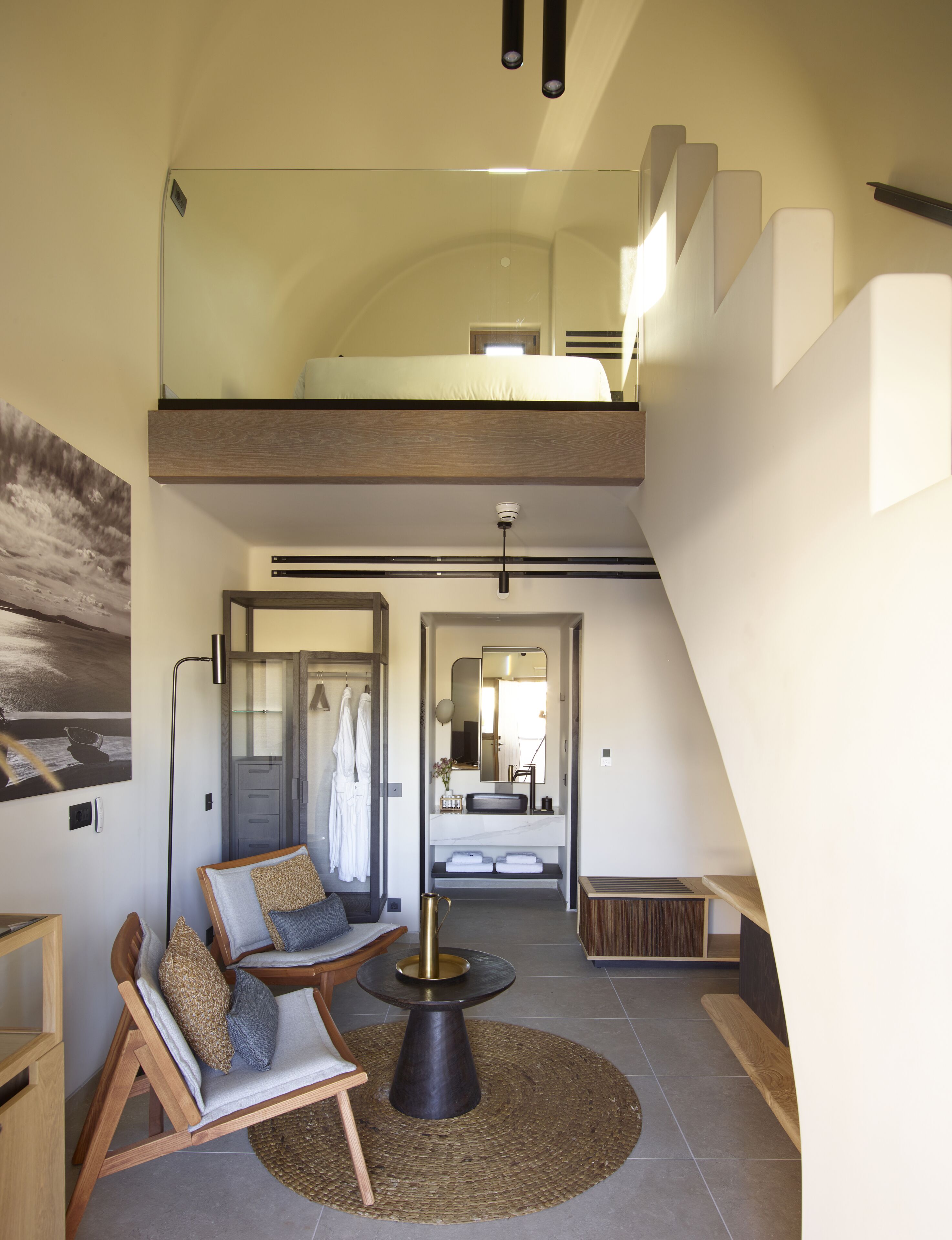 Un dormitorio estilo loft moderno con cama en entrepiso, zona de comedor con mesa redonda y baño con espejo grande.
