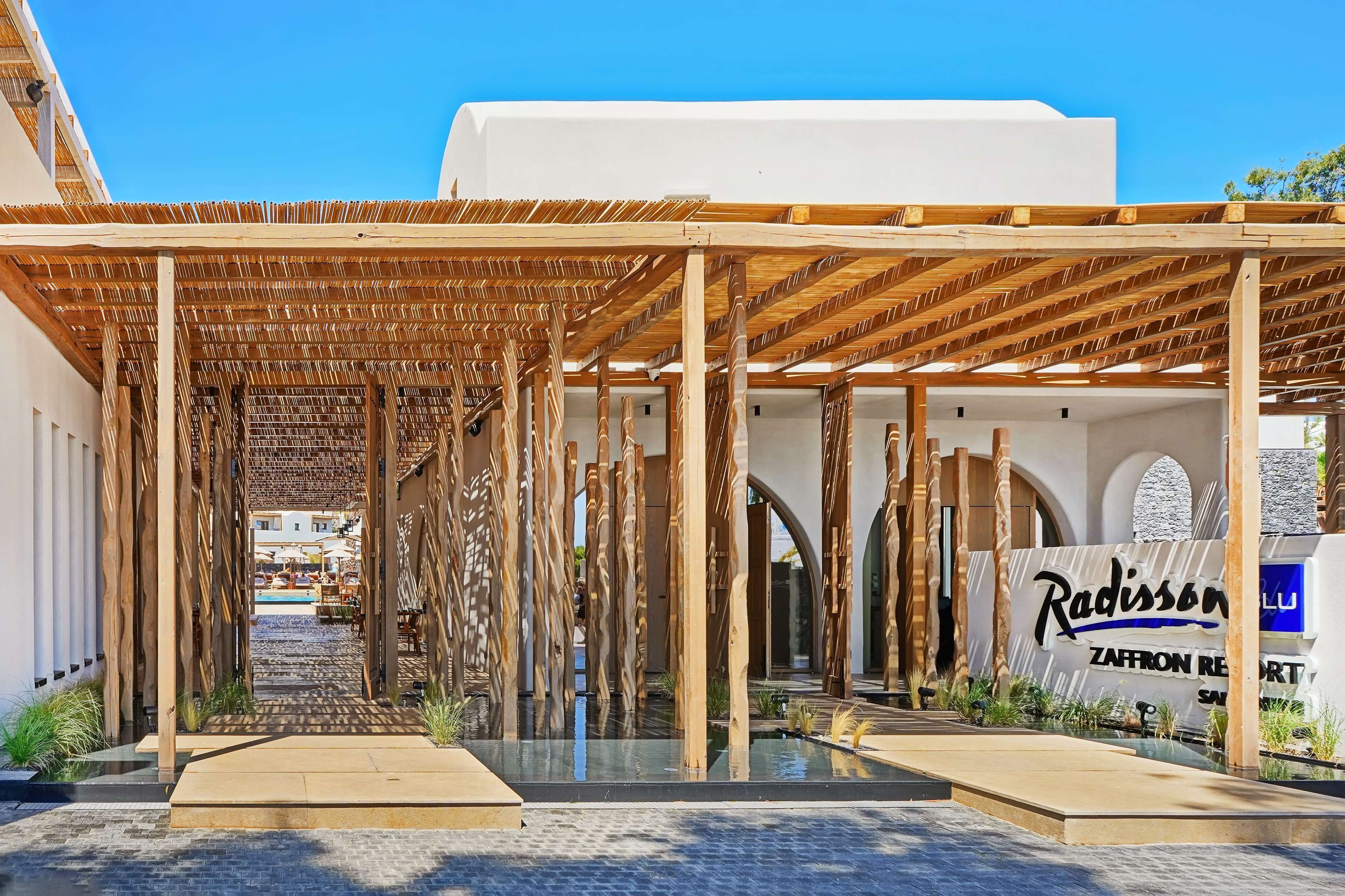 Un espacio al aire libre cubierto con vigas de madera y una piscina, que conduce a un edificio con un letrero que dice "Radisson Zafron Resort".